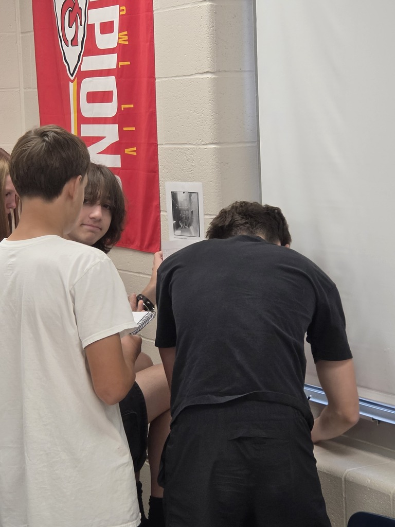 Three individuals, two in white shirts and one in black, are looking at a banner in a hallway.