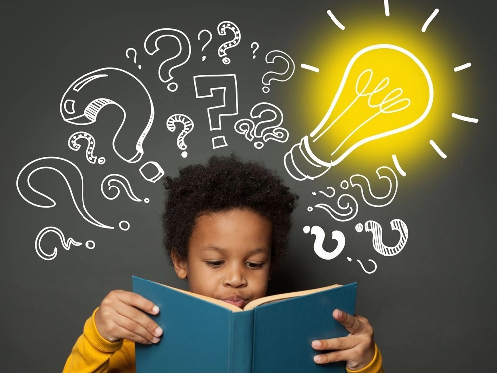 Child reading a book with drawings of question marks and a glowing light bulb above their head.