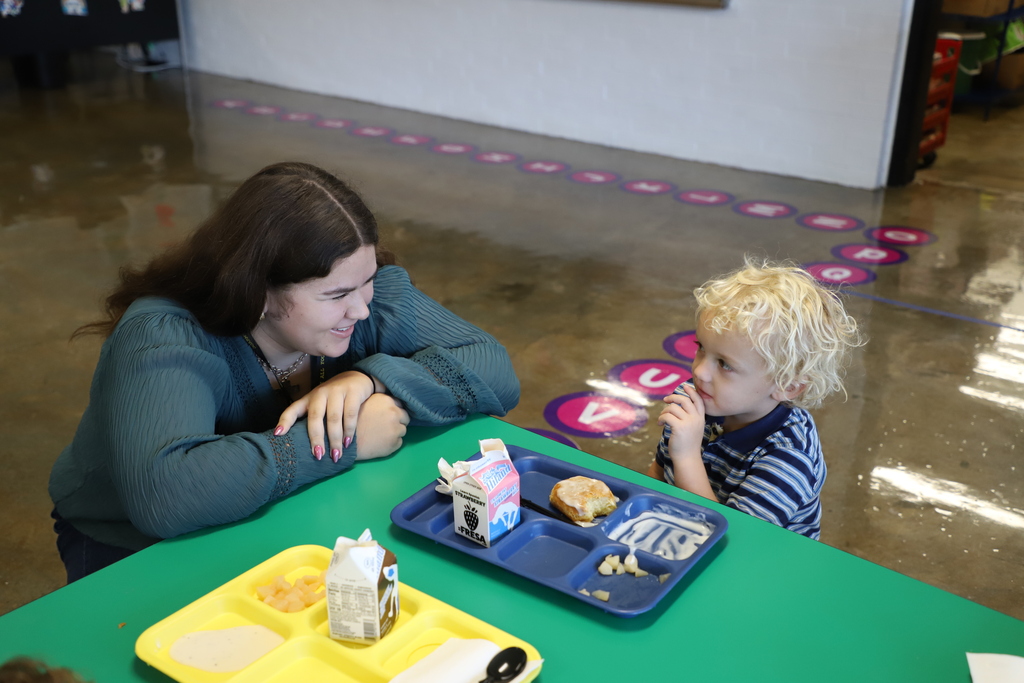 Attentive and encouraging. She's meeting him right at eye level while he navigates his lunch tray, complete with a biscuit and strawberry milk.