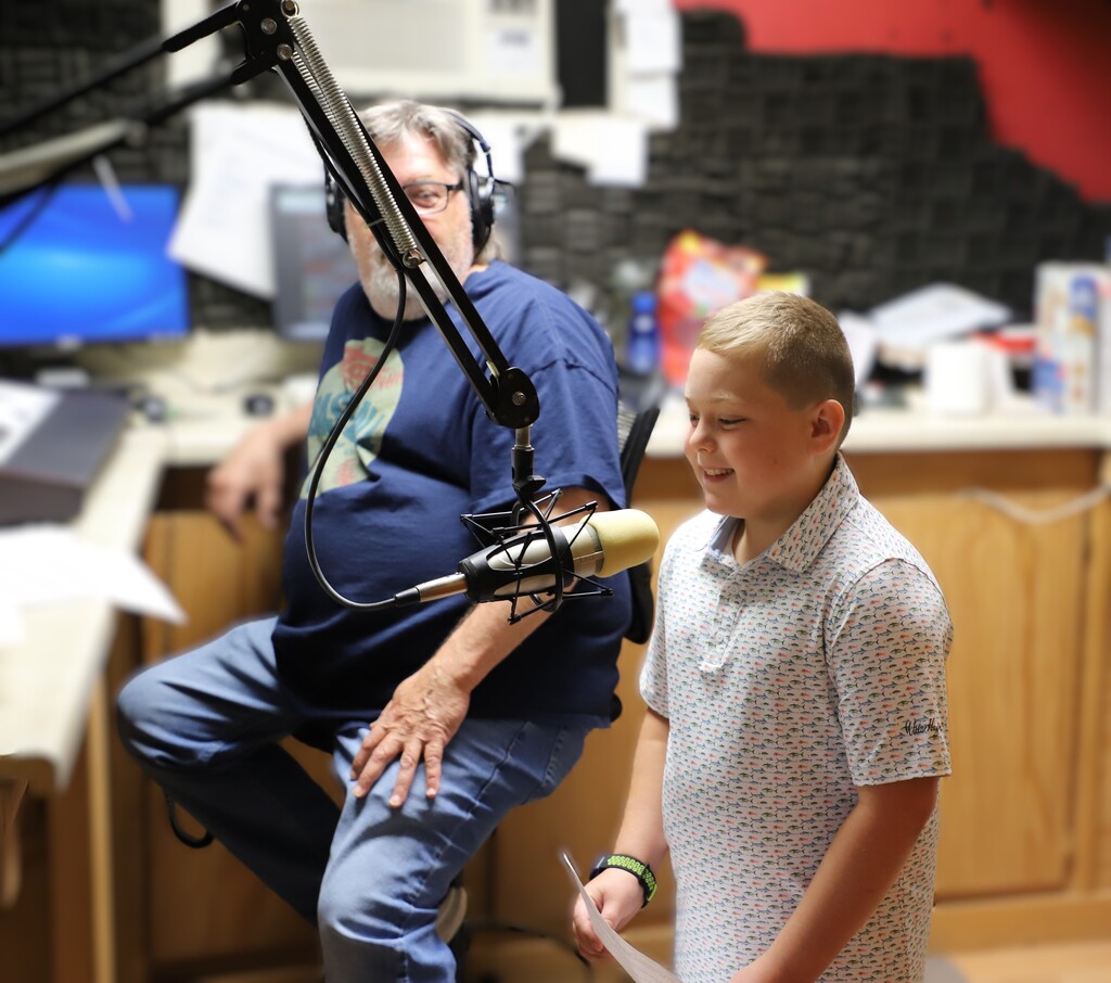Elementary student Oliver Mathis holding a script and speaking into a microphone in the ESPN radio studio.