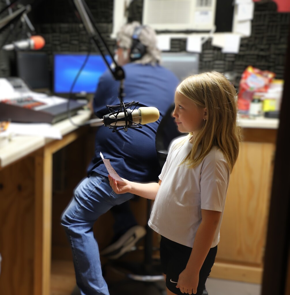 Young female student Olivia Reeves standing at a microphone in a radio recording studio while holding a script.