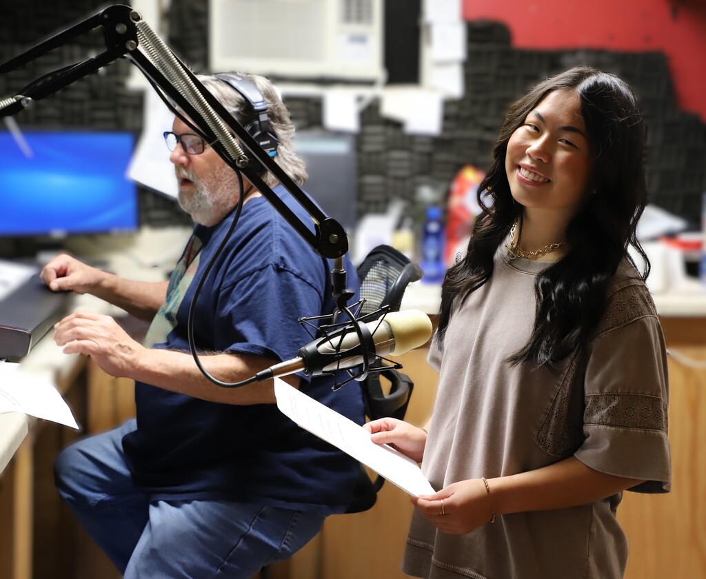 High school student Stevie Jones smiling next to a studio microphone with her script in hand during a radio recording session.