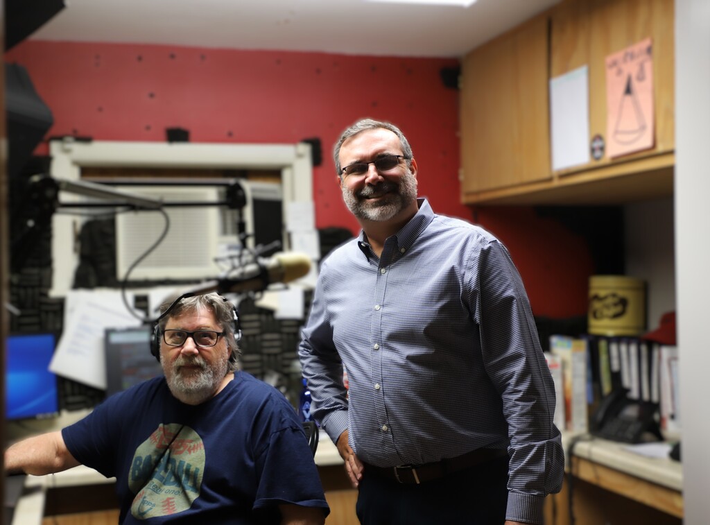 Forest Heights Elementary Principal Mark Ditmanson standing in the radio booth beside the radio host at his control console.