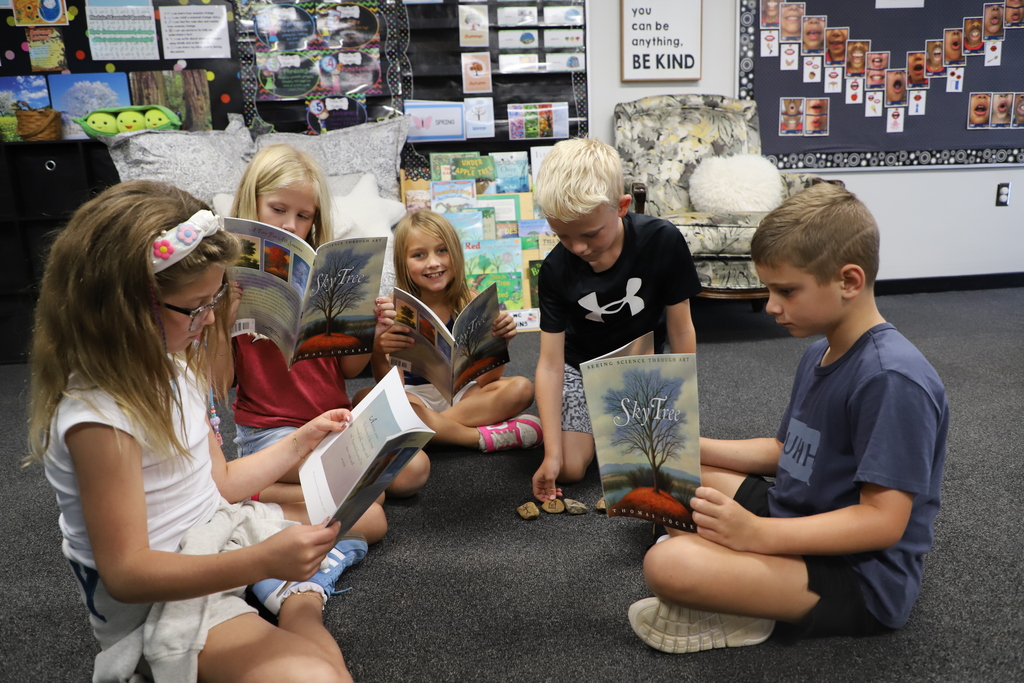 "Five elementary students sitting in a circle on a classroom floor, reading autumn picture books and placing story stones in the center."