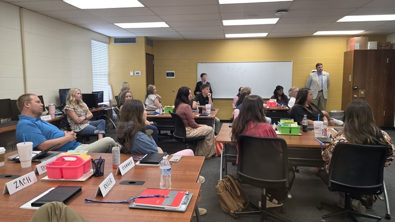 A room full of new Harrison Public Schools teachers and staff listening attentively during an inservice session, with Superintendent Dr. Stewart Pratt standing near the front of the classroom.