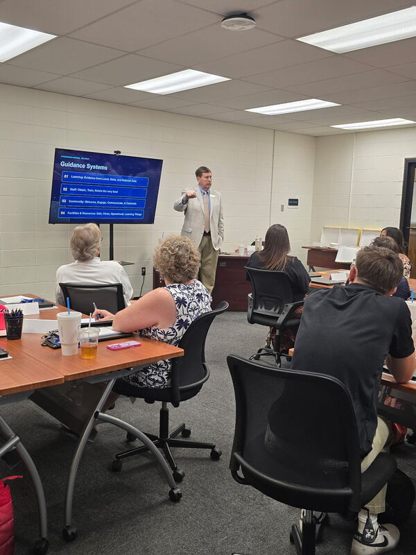 Harrison Public Schools Superintendent Dr. Stewart Pratt presents a slide titled "Guidance Systems" to new faculty and staff during inservice training at the Professional Development Center.