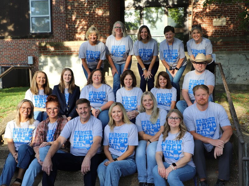 A group of 16 people wearing mathching grey shirts honoring Farmer Fred Days.