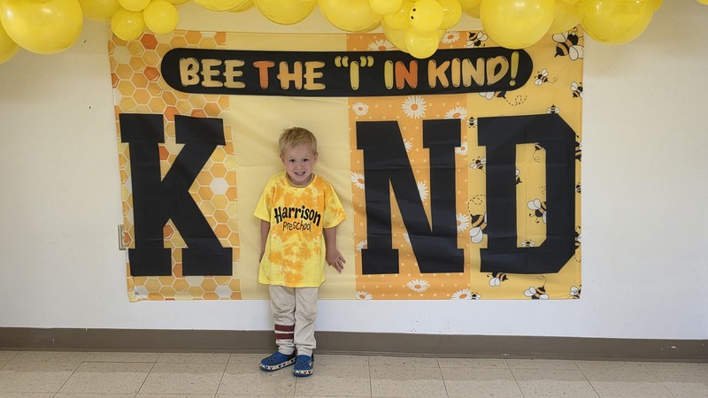 Student in photo backdrop  that says Bee the "I" in KIND.