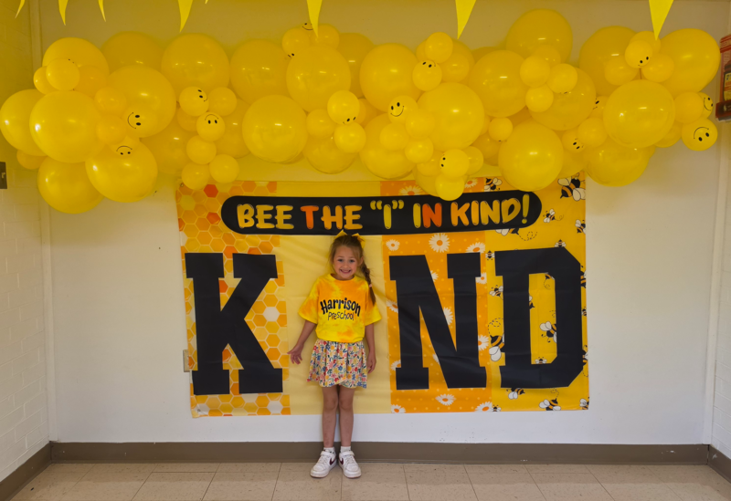 Student in photo backdrop  that says Bee the "I" in KIND.
