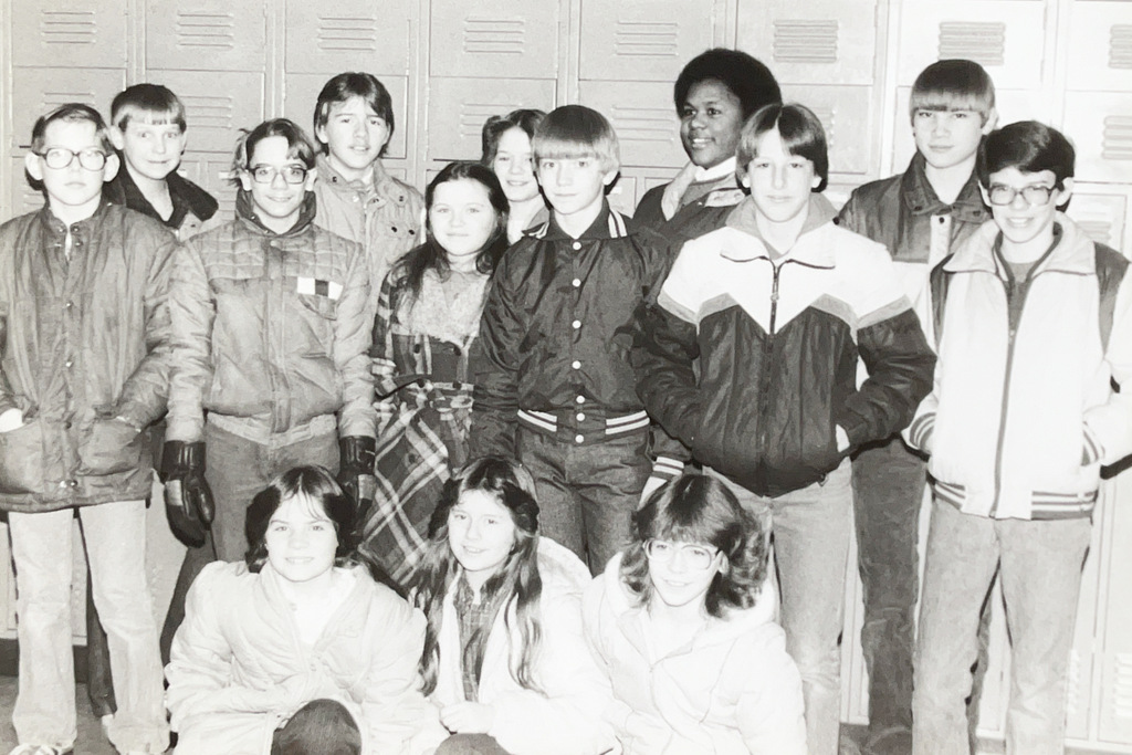 A group of middle school students poses together in front of hallway lockers for a class photo.