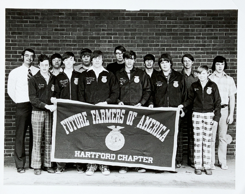 Hartford Future Farmers of America (FFA) chapter members and their advisor pose for a group photo holding the chapter banner outside a brick school building.