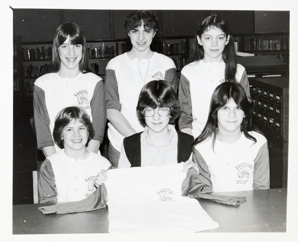 Black-and-white photo of six students posing in a school library, several wearing matching Hartford shirts.