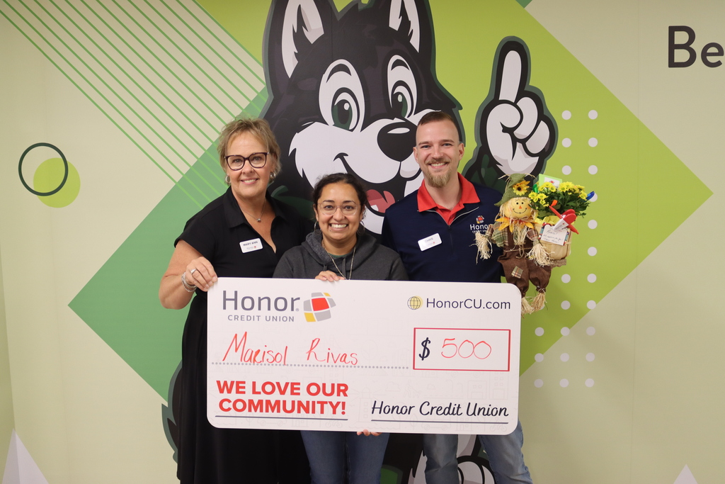 marisol rivas poses with honor credit union staff holding a big check that says $500 in front of the husky cartoon mural