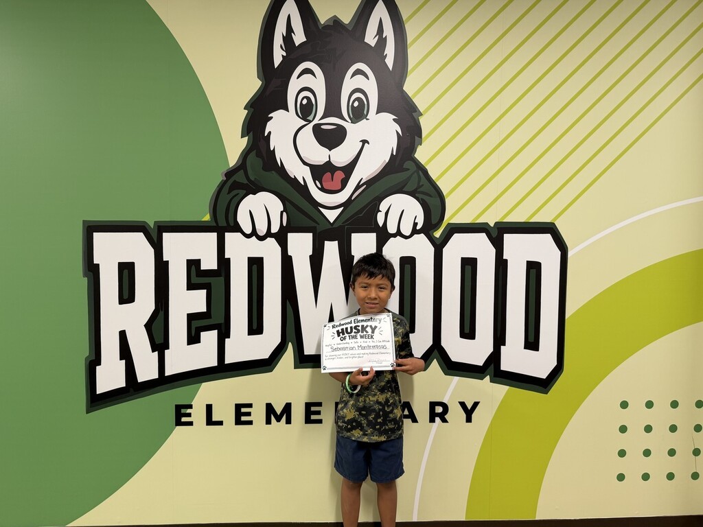 A Redwood Elementary student poses in front of the school’s Husky mural while holding his “Husky of the Week” certificate.