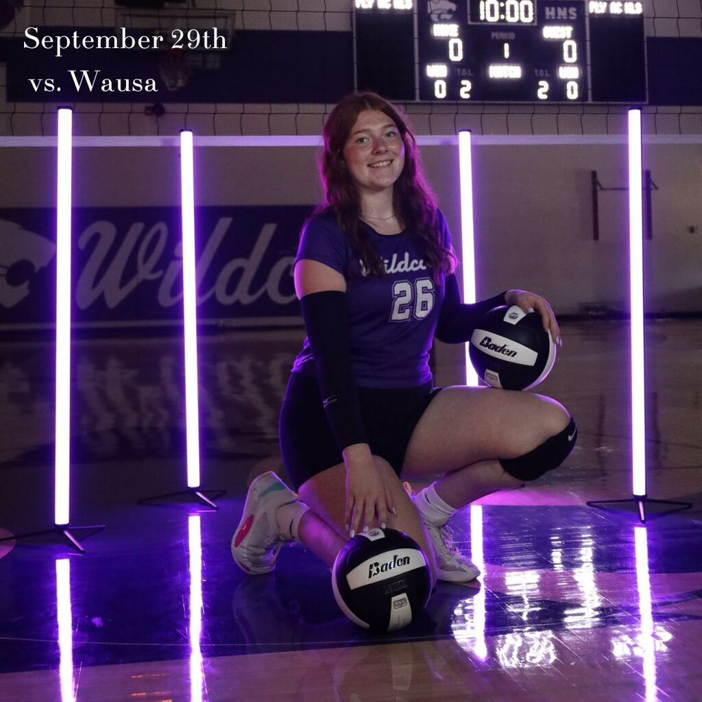 Volleyball player in purple No. 26 uniform kneels with two Baden balls under purple lights, smiling in a gym; text says September 29th vs. Wausa.