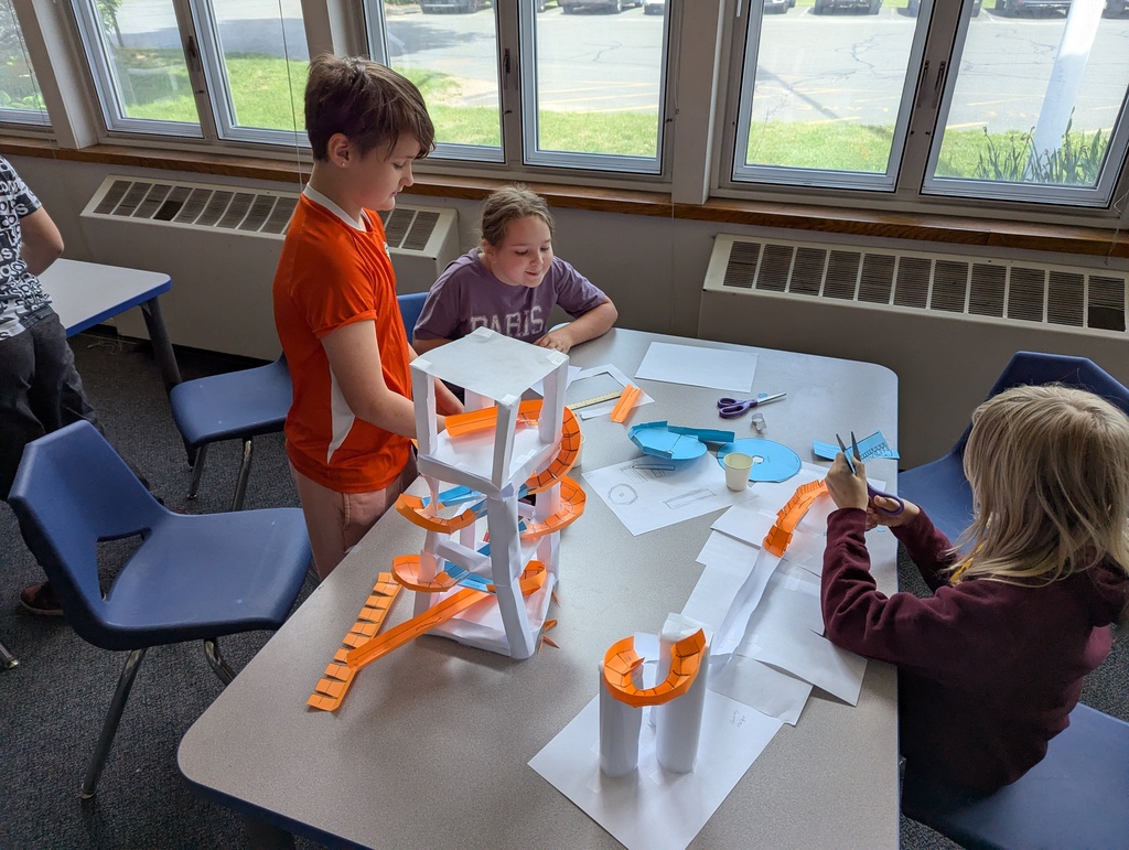 Girls all working on paper roller coaster on table.