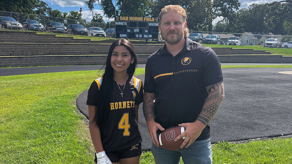 Coach and player stand on the football field.