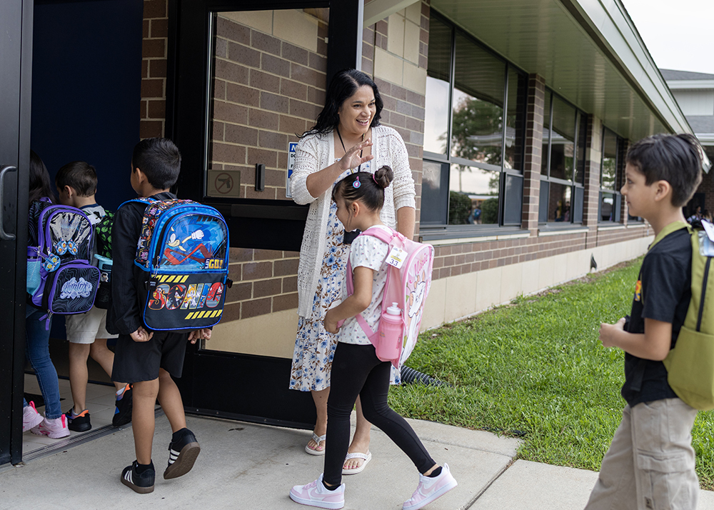 Staff member waves as students enter building