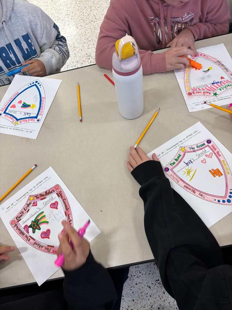 Students coloring and drawing on sheets of paper with shields printed on them!
