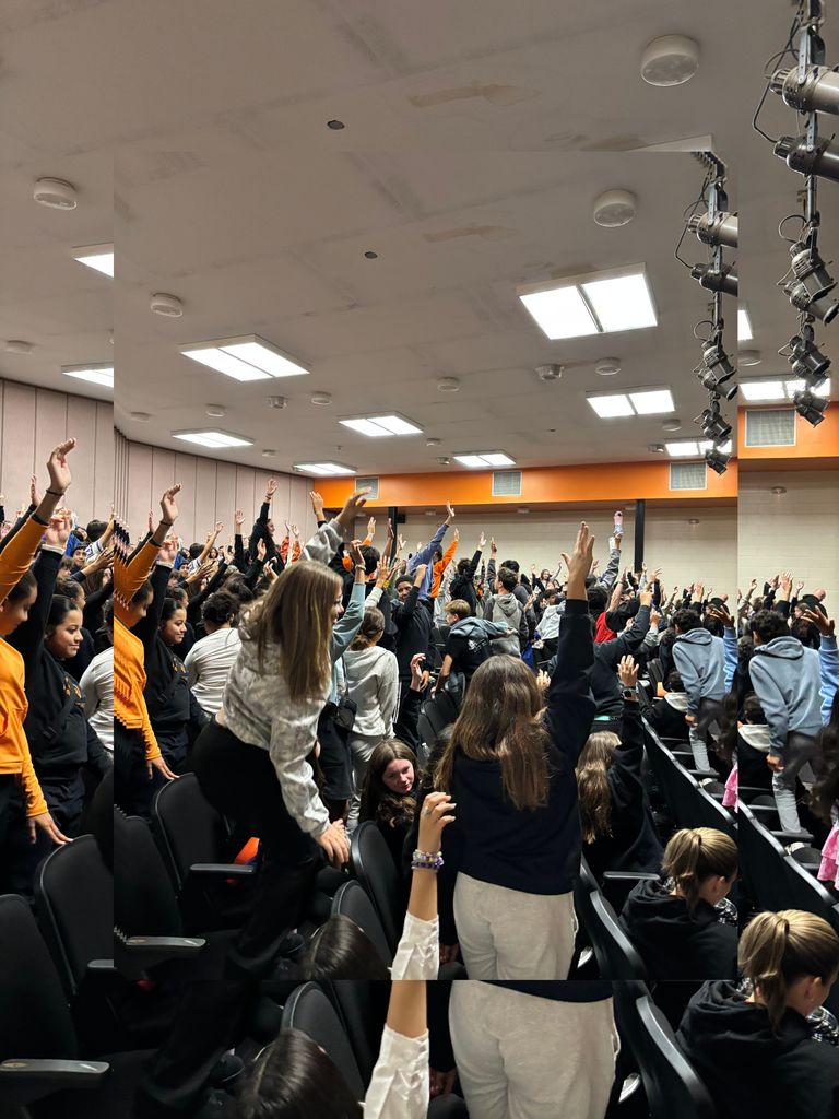 Students raising their arms as high as they can, some going as far as standing on top of auditorium chairs!