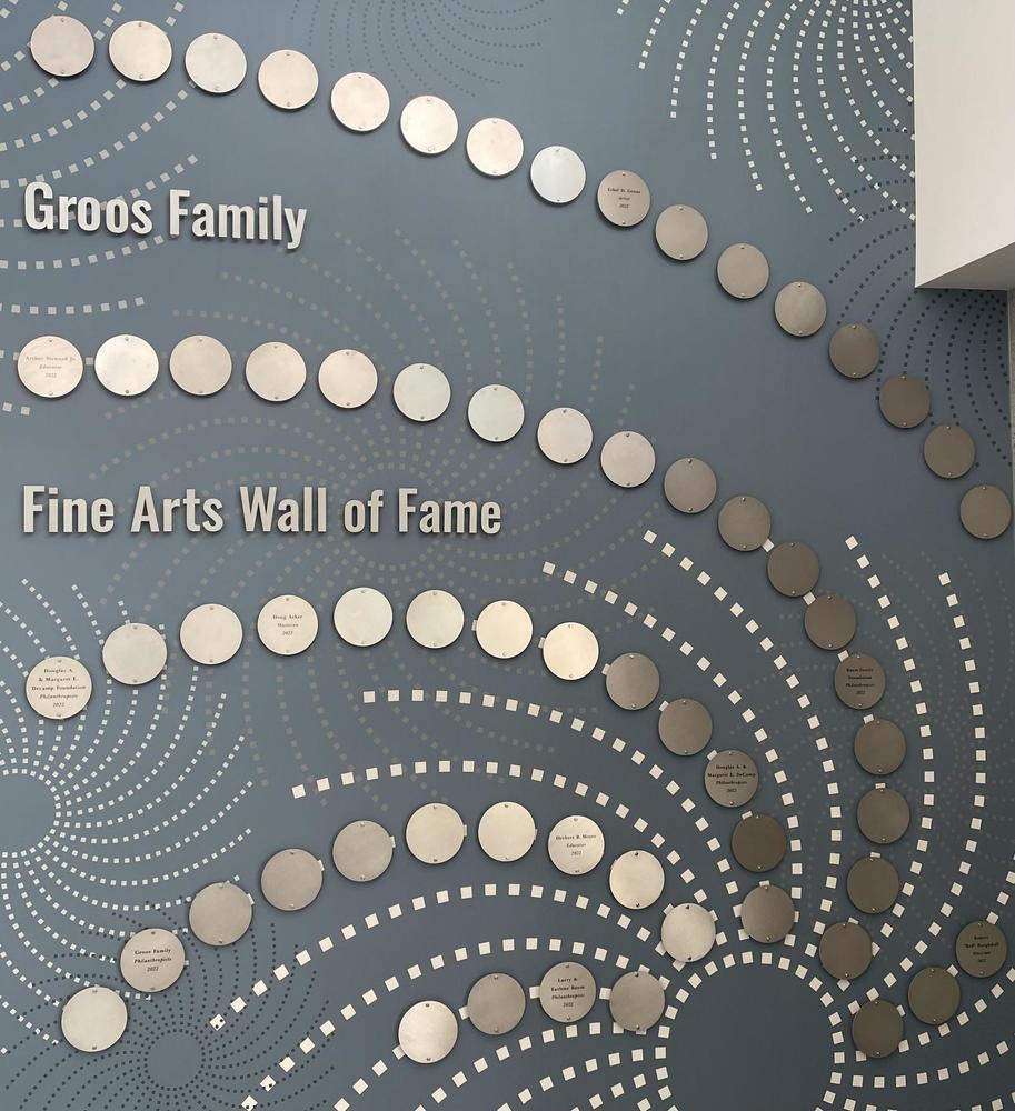 A wall covered with decorative plaques comprising the Groos Family Fine Arts Wall of Fame