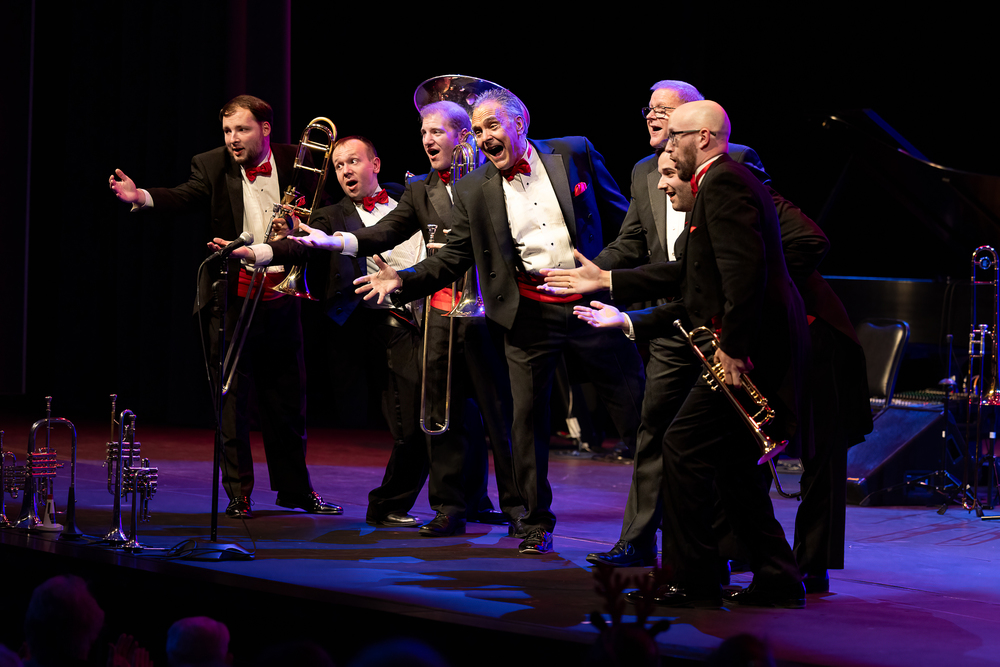 The King's Brass on stage, gesturing to the crowd while holding their instruments.
