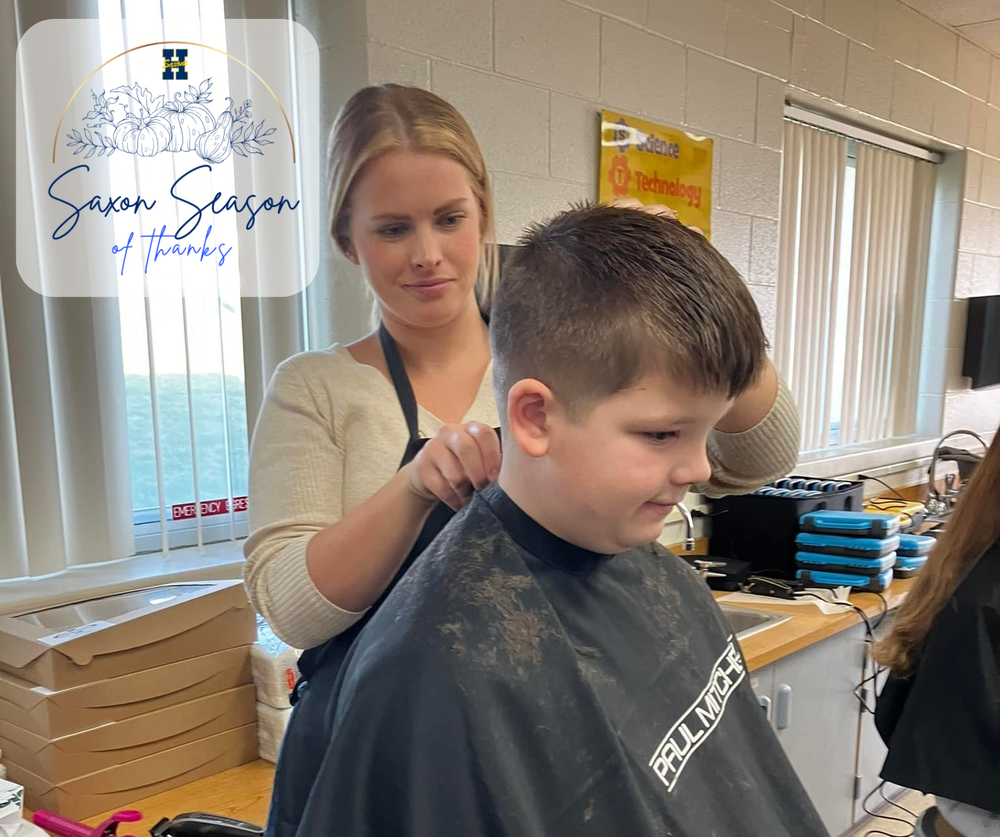 A female stylist runs a comb through the hair of an elementary school student, who is cloaked in a smock