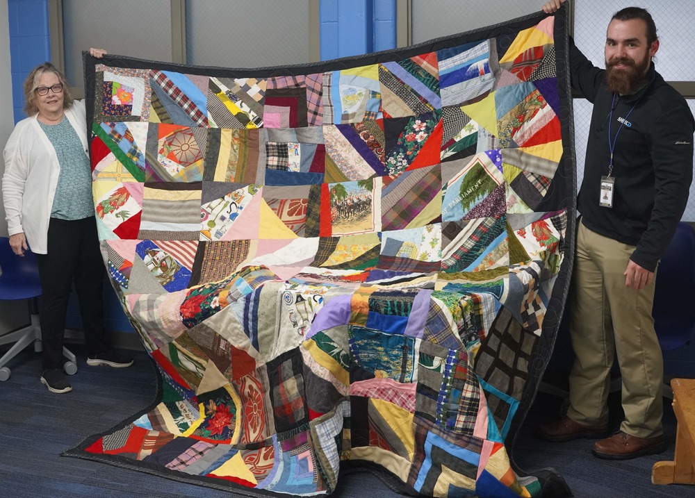 Two individuals hold up a quilt