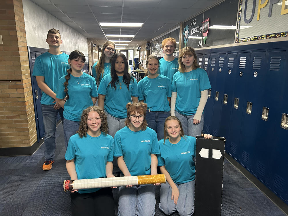 Students lined up for a photo, holding a large, novelty model of a cigarette