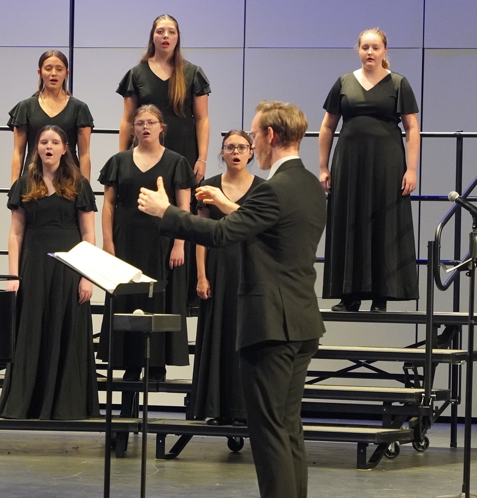 Mr. Moore directing a choir on stage at the Hastings Performing Arts Center.