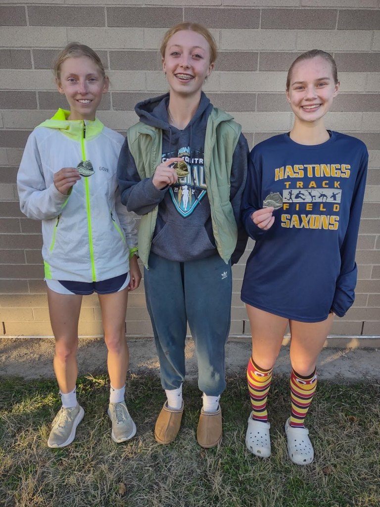 Hastings Saxon girls cross country runners displaying their all-county medals.