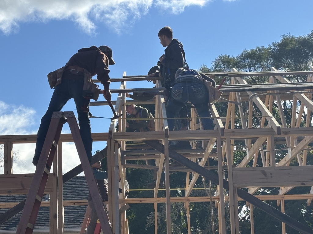 Hastings High School students are perched on the frame of a garage using tools to build.