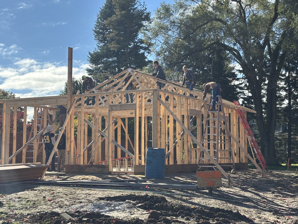 Hastings High School students are perched on the frame of a garage using tools to build.