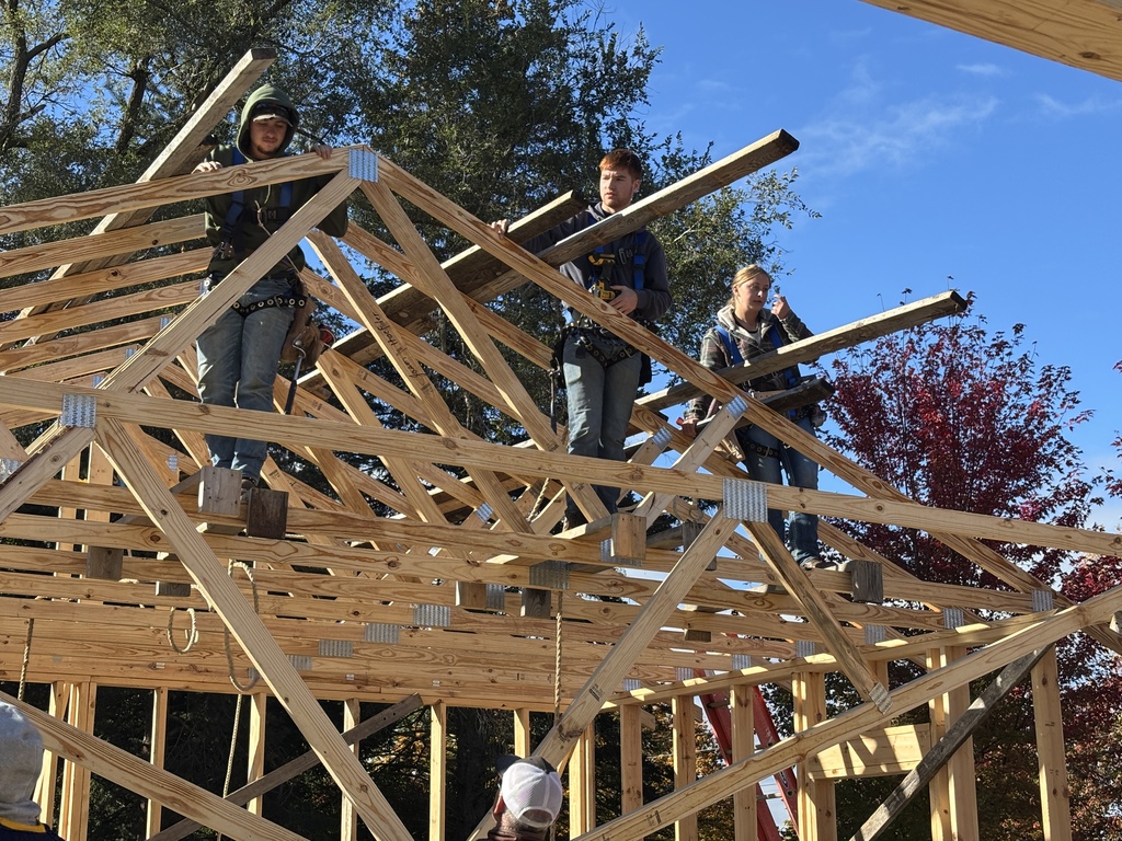 Hastings High School students are perched on the frame of a garage using tools to build.