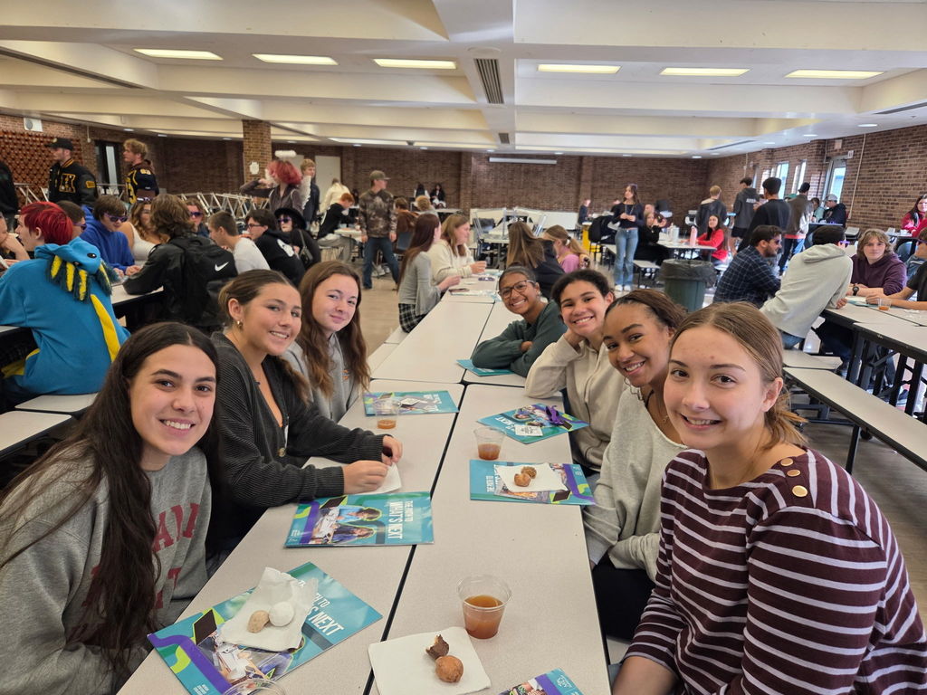 Several students posing and smiling as they sit at tables with donuts and cider.