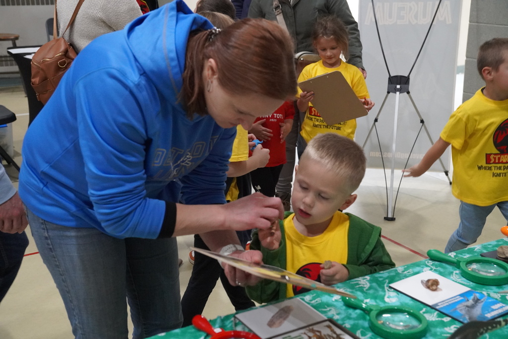 A parent bends down to examine a dinosaur display with a child.