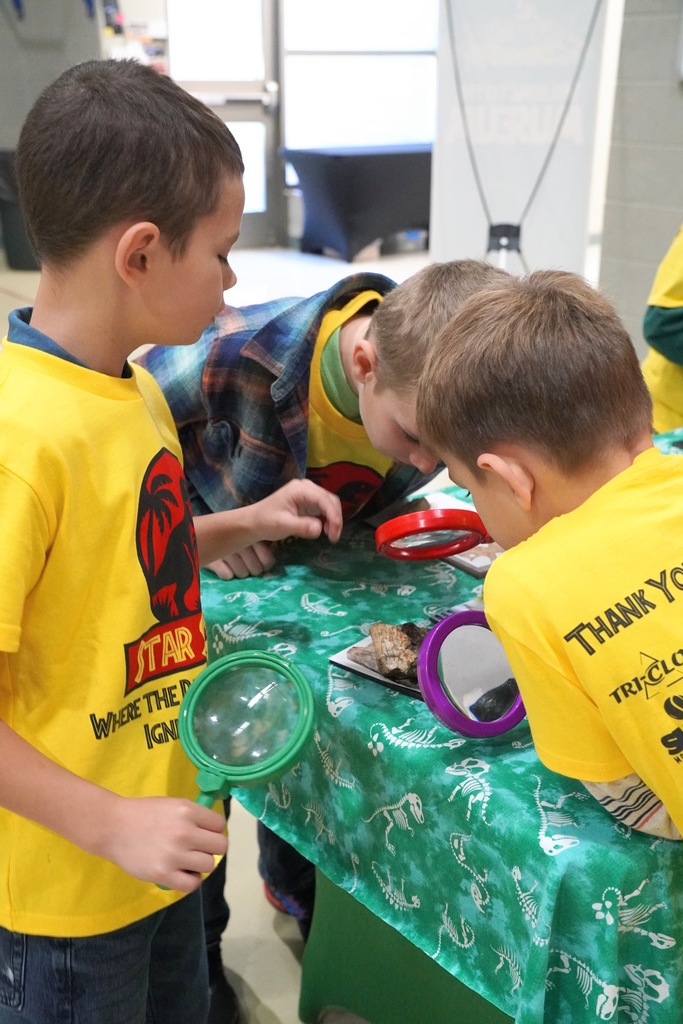 A group of students examine something with magnifying glasses.