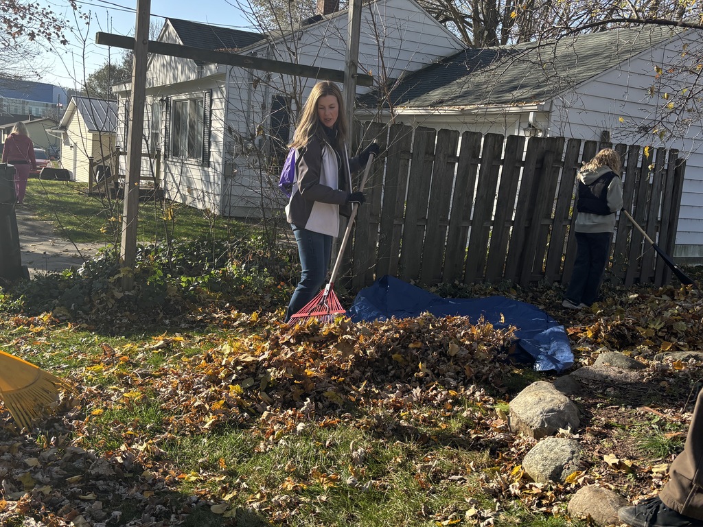 A woman rakes leaves with a fence in the background.