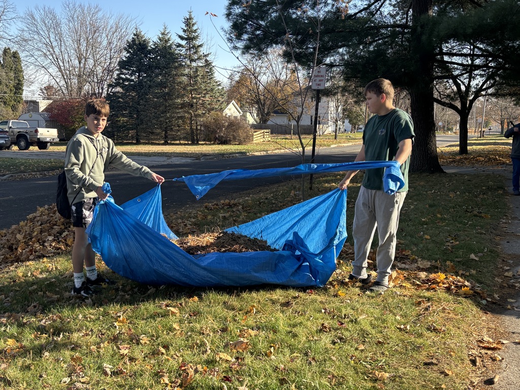 Two male students carry a blue tarp filled with leaves.