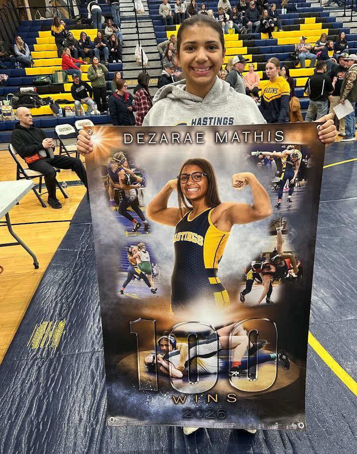 A girl stands holding a banner of herself celebrating 100 wins in wrestling.