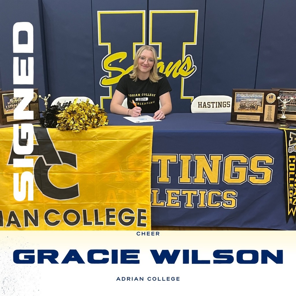 Gracie Wilson sits behind a table signing a piece of paper.
