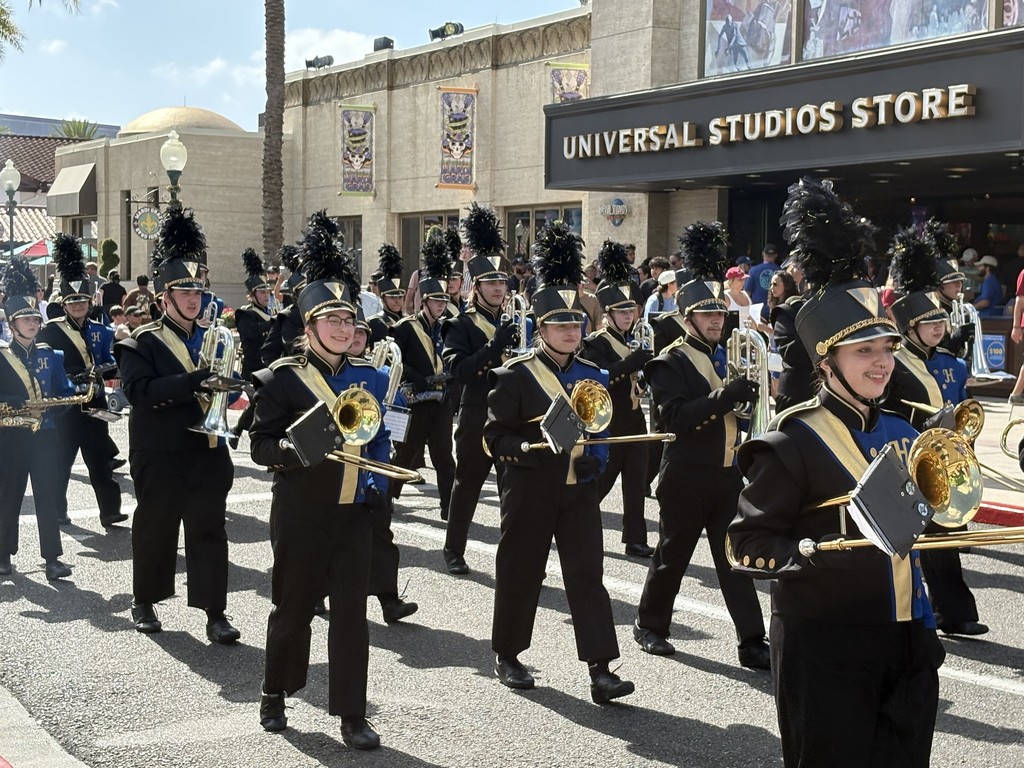 The Hastings March Band walks along the road. In the background is a building with a sign that says "Universal Studios Store"