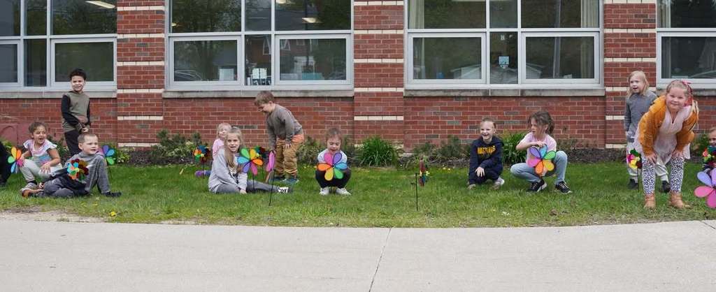 kids sticking pinwheel flowers into a grassy area outside of a school