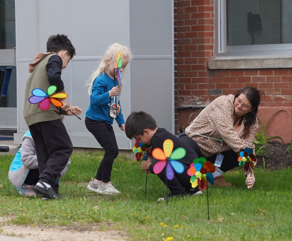 kids sticking pinwheel flowers into a grassy area outside of a school