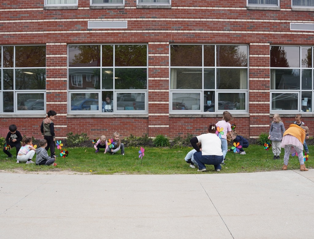 kids sticking pinwheel flowers into a grassy area outside of a school