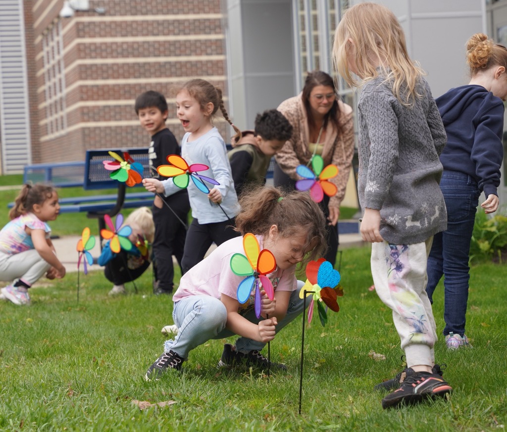 kids sticking pinwheel flowers into a grassy area outside of a school