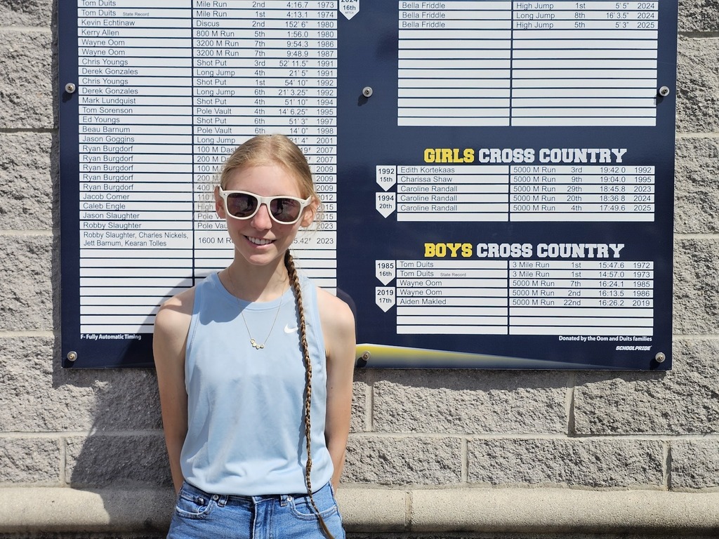 Caroline Randall stands next to the track record board and smiles.