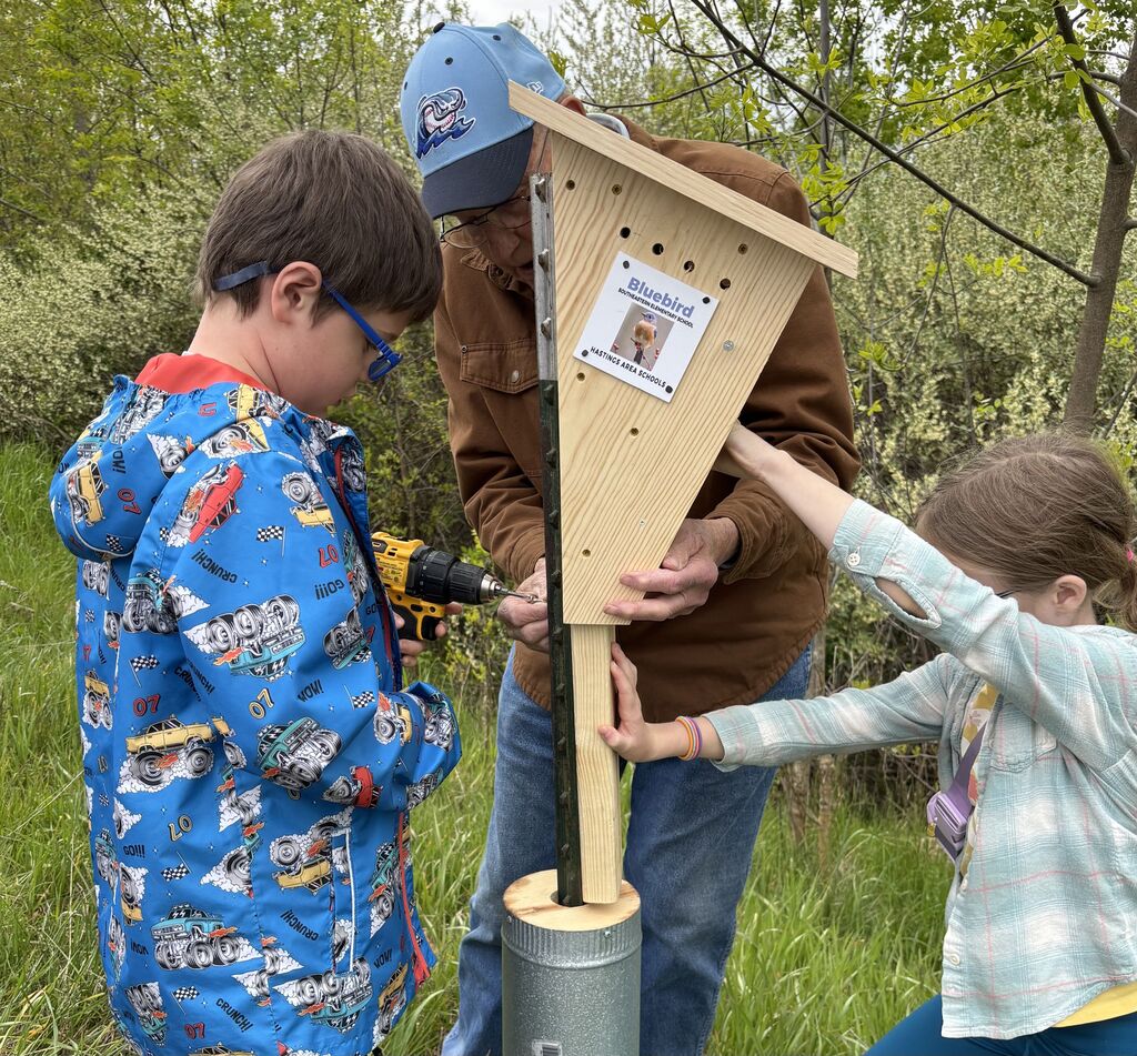 A group of kids setting up birdhouses under the watch of an elder individual