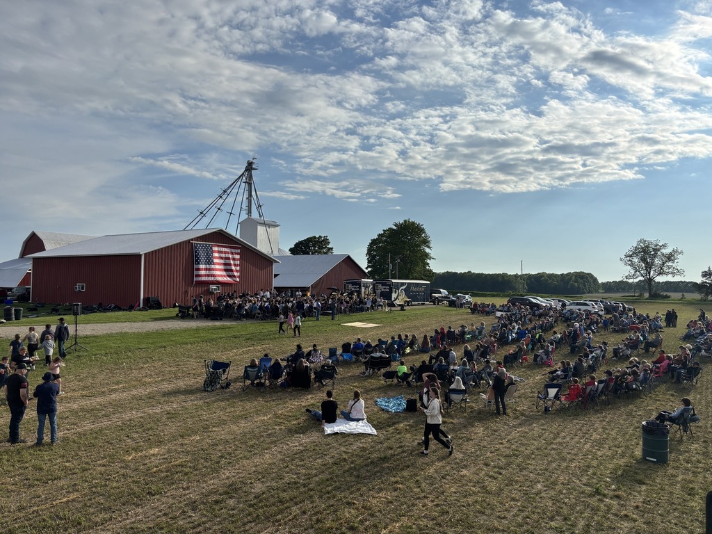 An aerial shot of many people seated in a hayfield with a full band seateed in front of them