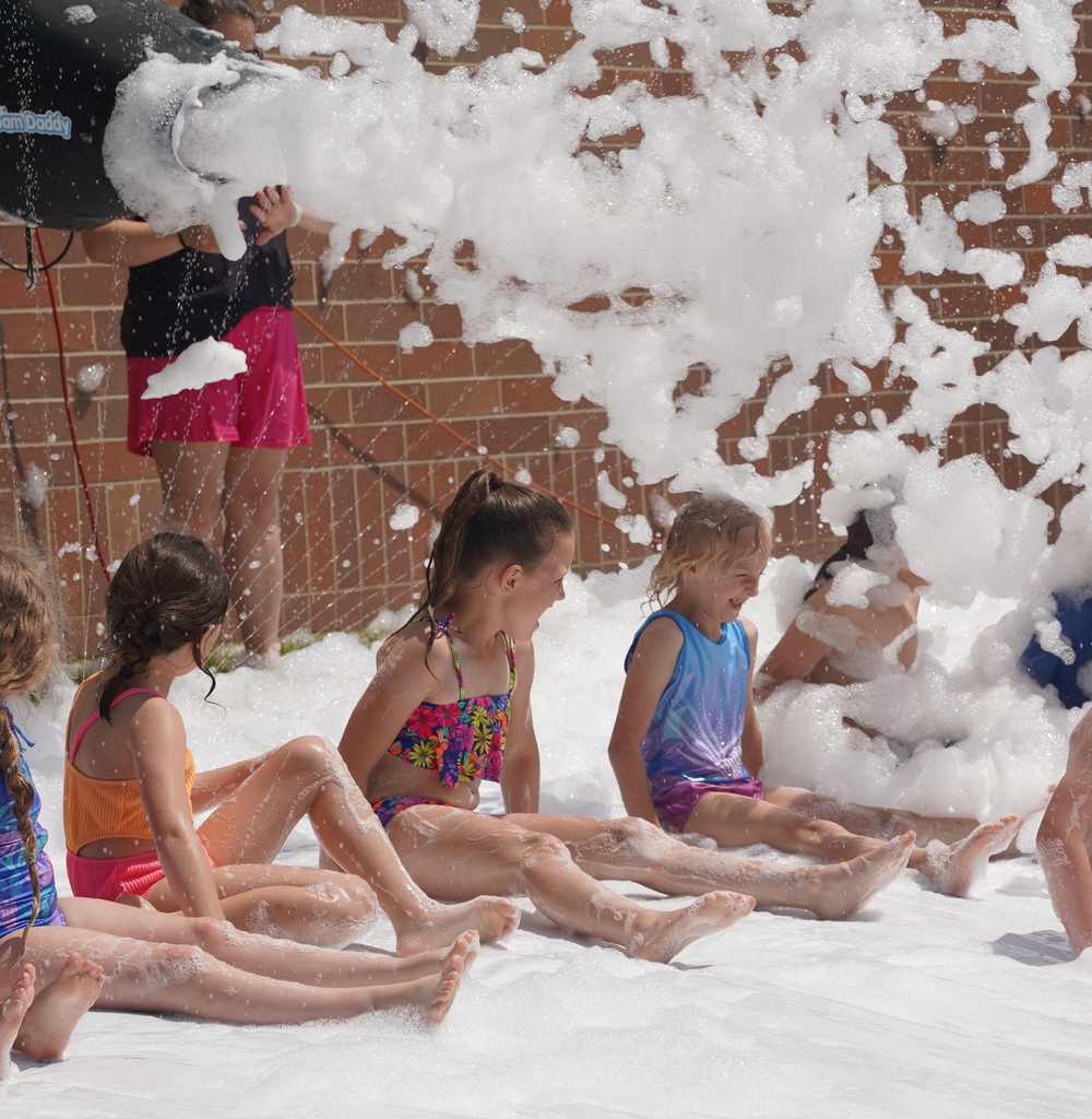 Kids play in foam and slide down a large tarp that is placed over a hill